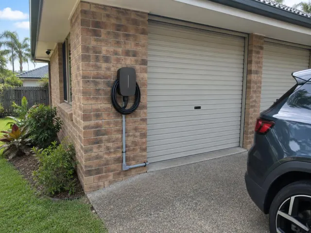 Wall-mounted EV charger on a brick exterior wall beside a garage door in Elanora