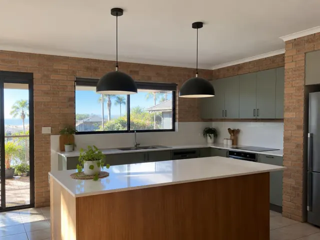 Modern kitchen with two black pendant lights over a white island and brick walls in Burleigh Heads